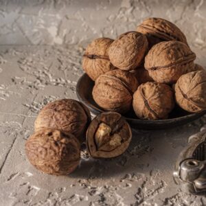 A rustic presentation of walnuts in a dish with a nutcracker on a textured background.